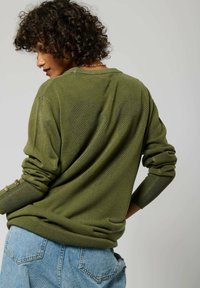 Maglione verde a maglia caratterizzato da un motivo a cuore testurizzato sulla parte posteriore, polsini a coste con dettagli in bottone e una vestibilità rilassata.