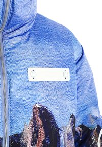 Chaqueta acolchada azul con un patrón texturizado que recuerda a montañas. Cuenta con una cremallera frontal y una etiqueta rectangular blanca de la marca.