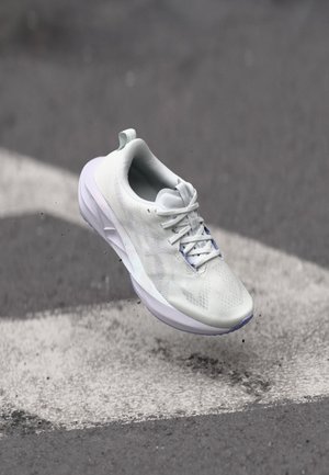 Scarpa sportiva bianca con tomaia texturizzata, design con lacci e suola imbottita. Gli accenti includono una suola esterna di un viola chiaro e una linguetta sul tallone.