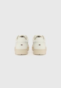 Paquet de baskets basses de couleur crème avec semelles beiges vues de dos, avec un petit logo rectangulaire rouge, blanc et bleu sur chaque talon.