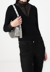 Maglietta nera a maniche lunghe con dettagli in pizzo sul collo e sui polsini, abbinata a jeans neri e una borsa a tracolla metallizzata argento.