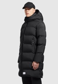 Sort pufferjakke med høj krave, lynlåslommer og et logo-patch. Glat, blank overflade med lagdelt, quiltet design.