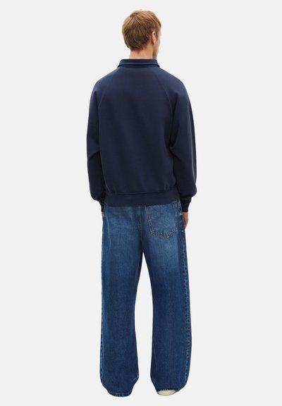 Felpa blu navy con colletto alto, polsini e orlo a costine, abbinata a jeans in denim azzurro oversize con tasca posteriore.