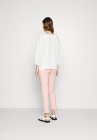 Vit långärmad blus med sammanknuta axlar, kombinerad med ljusrosa slimfit-byxor och vita sandaler med svarta sulor.