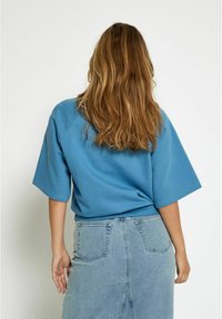 T-shirt in cotone blu a vestibilità rilassata con maniche corte, abbinato a una gonna in denim blu chiaro, dotata di tasche posteriori e orlo a mezza lunghezza.