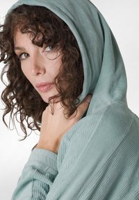 Prenda con capucha de suave tela texturizada en verde menta, con acentos de canalé en las mangas y un ajuste relajado alrededor de la cara.