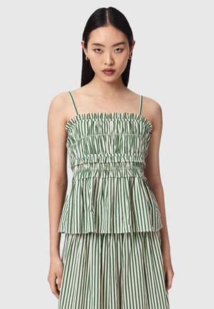 Femme portant un haut péplum sans manches à rayures verticales vertes et blanches avec de fines bretelles, accompagné d'un pantalon large assorti.