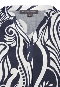 Blusa blu scuro con motivi bianchi a vortice, colletto a V, breve pattina con bottoni e texture di tessuto liscia. Etichetta del marchio visibile.