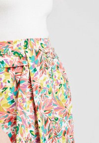 Jupe portefeuille florale dans des tons pastels de rose, vert et jaune. Elle présente une taille nouée et un tissu fluide avec un motif texturé.