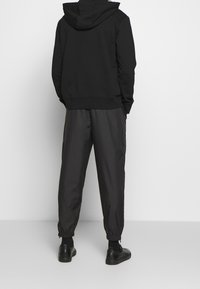 Černá mikina s kapucí na šňůrku, doplněná černými lehkými sportovními kalhotami. Oba kousky mají elastické detaily kolem manžet.