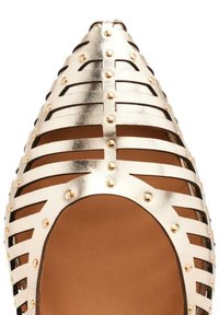 Zapato de punta afilada con diseño de recortes metálicos dorados, acentuado por clavos redondos y un interior marrón suave, creando un aspecto elegante y moderno.