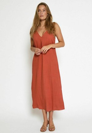Rust-colored maxi dress with a V-neck, spaghetti straps, and loose fit. Made from textured fabric, reaching mid-calf. Sandals visible below.