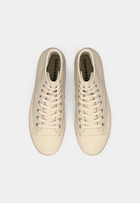 Beige hoge sneakers met een gladde textuur, platte veters, zilveren vetertjes en rubberen zolen. Heeft het "CONVERSE" logo aan de binnenkant.