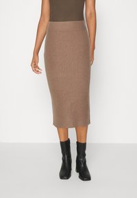Jupe midi en tricot côtelé de couleur marron chaud, avec une taille élastique et une silhouette droite, associée à des bottines noires.