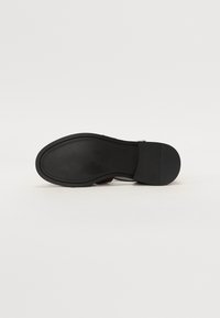 Czarna skórzana podeszwa buta o gładkim wykończeniu, zaokrąglonym kształcie i szczegółowym przeszyciu wzdłuż krawędzi. Minimalistyczny design bez wzorów.
