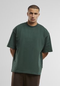 Zöld, oversized póló, puha pamutból készült, kerek nyakkivágással és rövid ujjakkal, laza szabású, oldalsó címkebelső részletet tartalmaz.