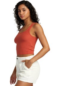 Rust-colored ribbed sleeveless crop top paired with white corduroy shorts featuring front pockets and button closure.