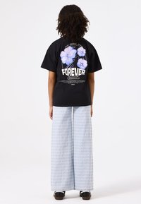 Camiseta negra con un gráfico floral colorido y la palabra "FOREVER" en la parte posterior, combinada con pantalones de pierna ancha de patrón azul claro.