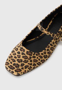 Shoe plano com padrão de leopardo, com biqueira quadrada e uma tira preta fina ao longo do peito do pé, apresentando um material superior suave e texturizado.