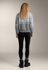 Šedý pletený svetr s geometrickými vzory v modré a bílé barvě, doplněný černými legínami a černými zimními botami. Texturovaná látka, ležérní střih.