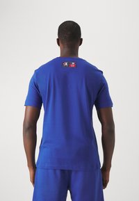 Modré bavlněné tričko s krátkými rukávy, s logem na zadní straně krku. Hladká textura a klasický kulatý výstřih.