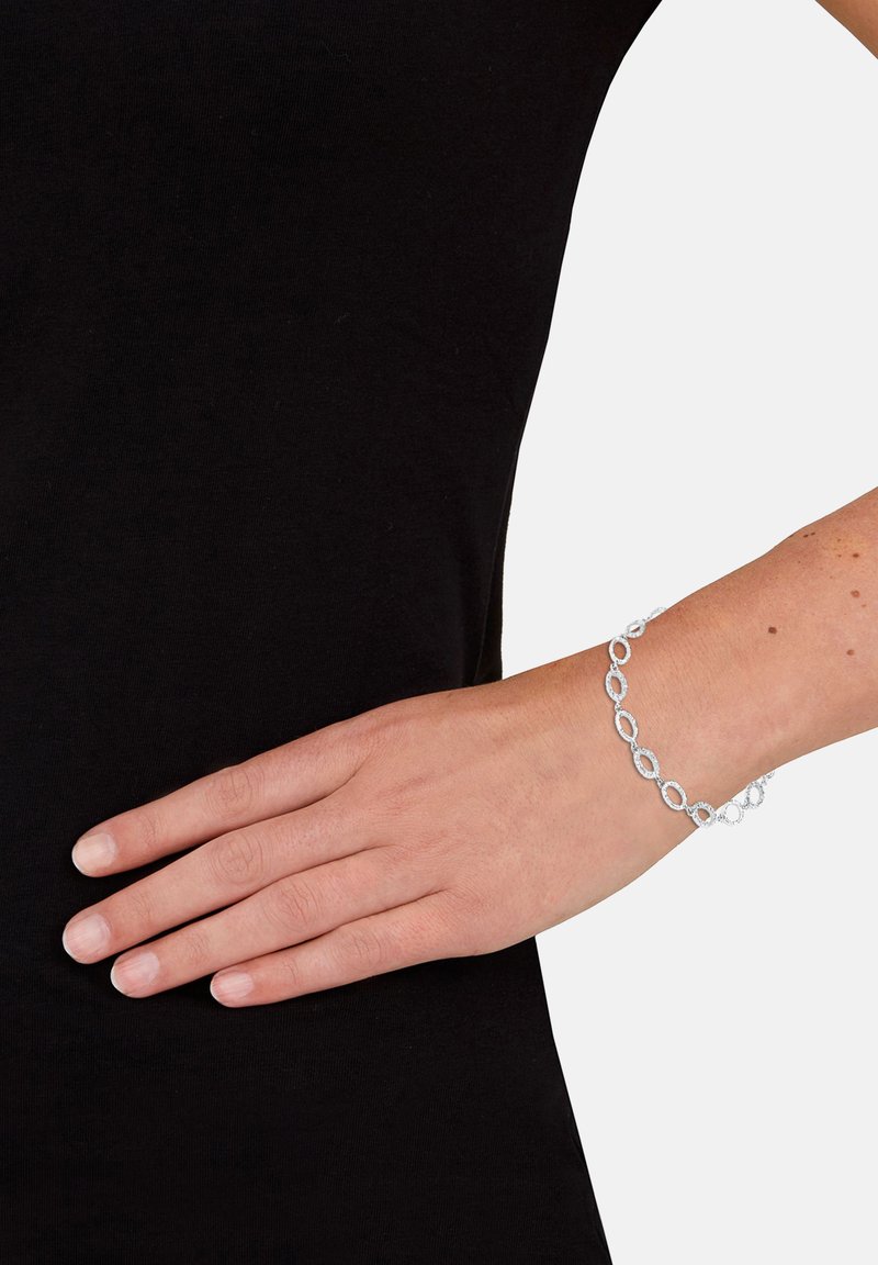 Silverfärgad armbandskedja med avlånga ovala länkar med en strukturerad yta, bärs på en hand mot en svart bakgrund.