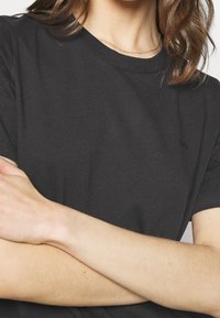 Kortärmad svart bomullströja med rundad hals och subtil logotypdetalj på bröstet, med en slät yta och avslappnad passform.