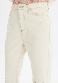 Vaqueros de tiro alto en beige, confeccionados en denim con un ligero stretch, que presentan detalles desgastados, costuras en color naranja y un cierre clásico de botón.