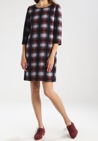 Robe à carreaux avec des manches trois-quarts en bleu marine, rouge et blanc. Fabriquée en tissu texturé avec une coupe droite. Associée à des chaussures bordeaux.