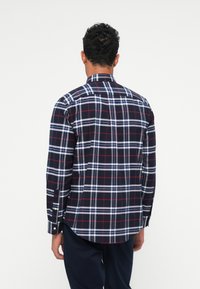 Camicia a quadri navy con motivi a scacchi rossi e bianchi, colletto button-down, maniche lunghe e orlo curvo. Realizzata in tessuto intrecciato.