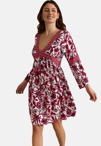 Robe à imprimé floral avec des manches longues, un décolleté en V profond et une silhouette évasée. Présente des fleurs rouges et roses sur un fond blanc.