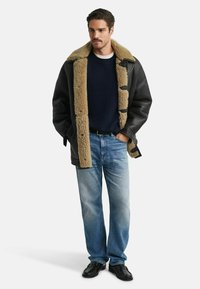 Černá kožená bunda s krémovým beránkovým límcem, námořnický svetr, světle modré džíny a černé boty. Bunda má zapínání na kalíšky a volný střih.