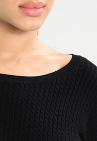 Maglione nero a maglia con un design a trecce testurizzate, ampio collo a giro e bordi a coste. Tessuto morbido con un aspetto liscio.
