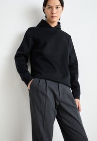 Black striped hoodie with a high collar, paired with gray pinstripe trousers. Both pieces feature soft textures and a relaxed fit.