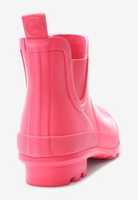 Botte de pluie en caoutchouc rose à la cheville avec une semelle texturée et une sangle de tirage, arborant un logo de montagne embossé sur un fond blanc uni.