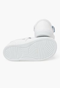 Sneaker bianche con tomaia in pelle liscia, cinturino in Velcro e suola in gomma testurizzata caratterizzata da dettagli a righe e un logo circolare.