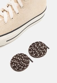 Beige Leinensneaker mit runden, geflochtenen braunen Schnürsenkeln mit weißen Sprenkeln. Der Sneaker hat eine Gummisohle und cremefarbene Schnürsenkel.