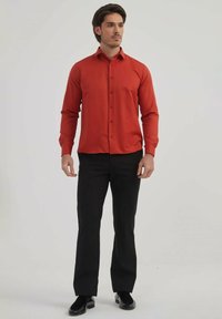 Chemise longue à manches rouges avec un devant à boutons, assortie à un pantalon noir. La chemise est faite d'un tissu lisse et présente une coupe ajustée.