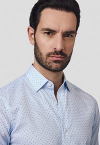 Jasnoniebieska koszula zapinana na guziki z delikatnym wzorem kropek. Posiada standardowy kołnierzyk i guziki, uszyta z gładkiego materiału.