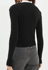 Czarny sweter prążkowany z długimi rękawami i dopasowanym krojem, zestawiony z szarymi dżinsami o tylnej kieszeni i teksturowanym wykończeniu.