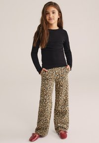 Maglietta nera a maniche lunghe abbinata a pantaloni larghi in stampa leopardata nei toni beige, marrone e nero. I pantaloni presentano un tessuto morbido e testurizzato.