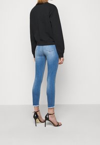 Svart cropped sweatshirt, figurnära ljusblå skinny jeans med fransade kanter, och svarta stilettklackar, sedd bakifrån.