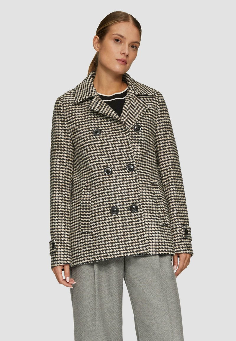 Kaksirivinen takki mustavalkoisessa houndstooth-kuosissa, jossa on suuret napit, leveä kaulus ja sivutaskut. Pehmeä tekstuuri.
