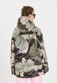 Wasserdichte Jacke mit Kapuze, ausgestattet mit einem abstrakten Muster in Grün-, Braun- und Violetttönen. Lockerer Schnitt mit einem subtilen Glanz und verstärkten Nähten.