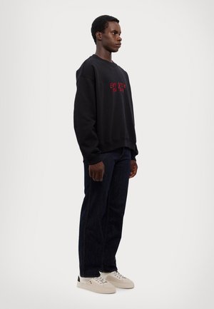 Black sweatshirt with red text reading "Every Smile You Take," paired with dark blue denim jeans and white sneakers with a black accent.