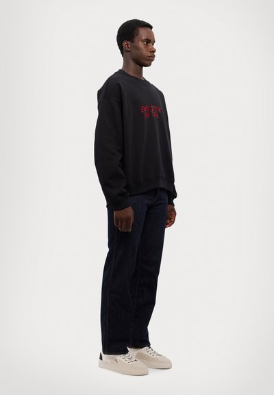 Schwarzer Hoodie mit rotem Text "Every Smile You Take", kombiniert mit dunkelblauen Jeans und weißen Sneakers mit schwarzem Akzent.