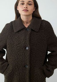 Bruine, getextureerde wollen jas met grote kraag, knopen aan de voorkant en zijzakken. Het materiaal heeft een vlezige uitstraling en biedt warmte.