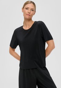 Czarny krótki top z krótkim rękawem o prążkowanej strukturze i okrągłym dekolcie, w zestawieniu z dopasowanymi czarnymi spodniami. Minimalistyczny design i luźny krój.