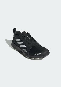 Scarpa da ginnastica nera con tomaia in mesh testurizzato, tre strisce argentate e un dettaglio di design numerico. Presenta una suola in gomma durevole con trazione.