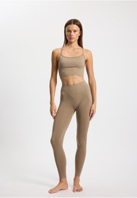 Béžový sportovní crop top a odpovídající legíny s vysokým pasem, vyrobené z pružného materiálu s hladkou texturou a minimálními švy, s tenkými ramínky.